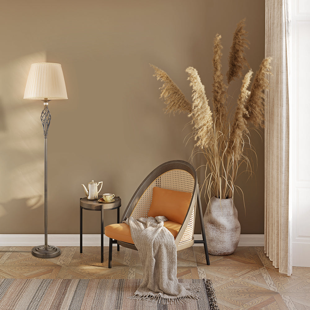 Mise en ambiance salon, lampadaire allumé près d'un fauteuil cannée et d'un vase de roseaux