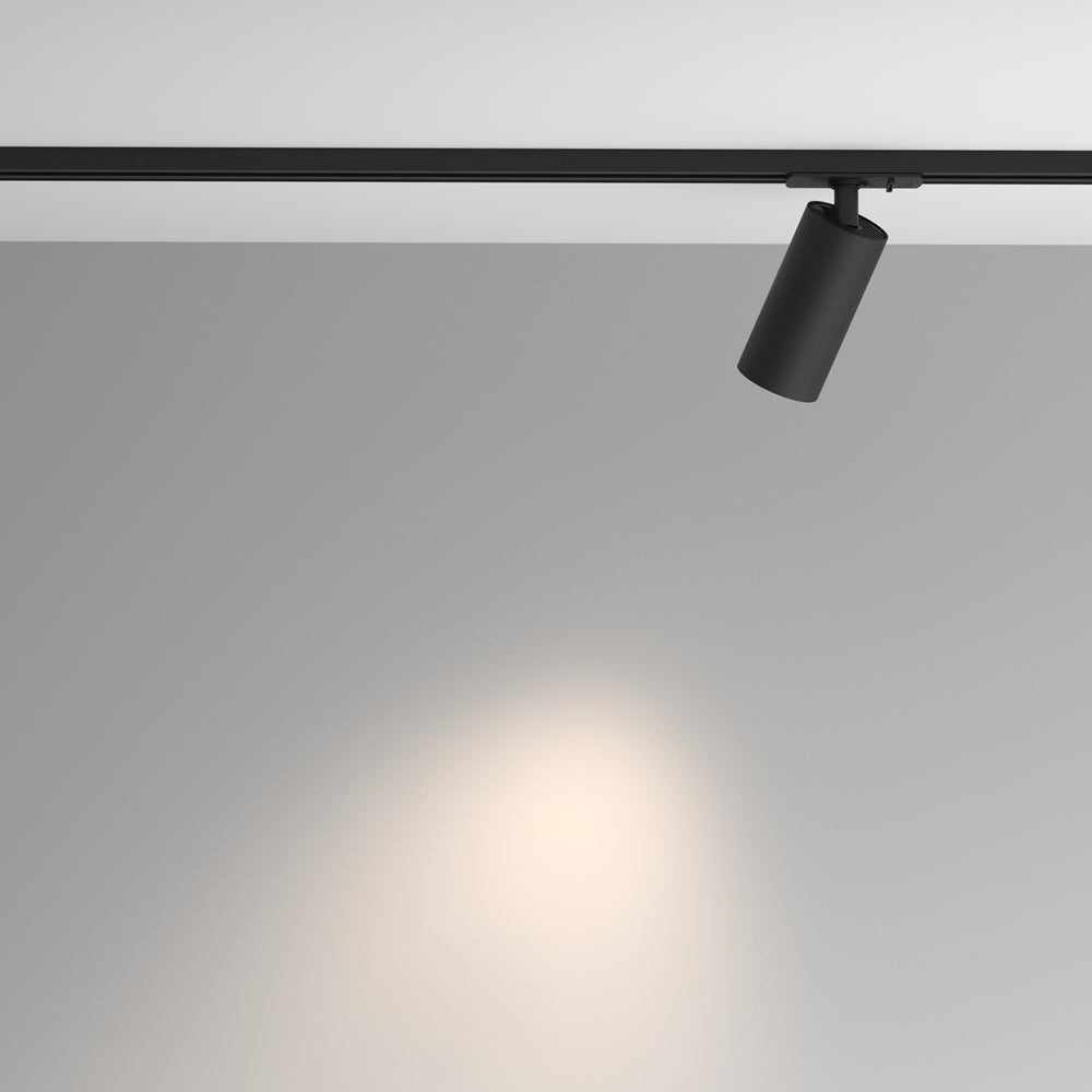 Spot noir sur rail fixé au plafond, éclairant un mur gris