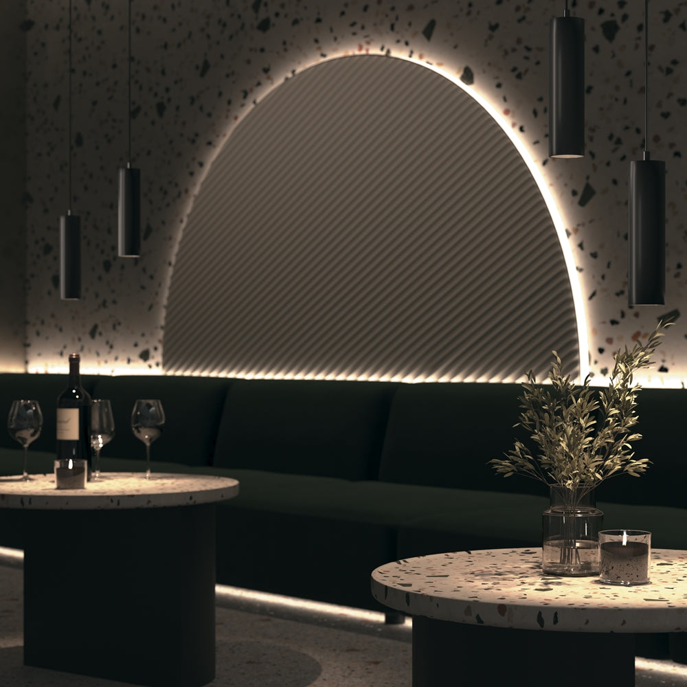 Scène d'intérieur de bar avec plusieurs suspensions noires au-dessus de tables en terrazzo.