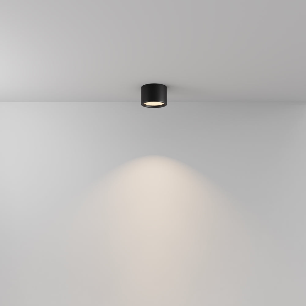Plafonnier cylindrique noir au plafond, halo de lumière chaude sur le mur