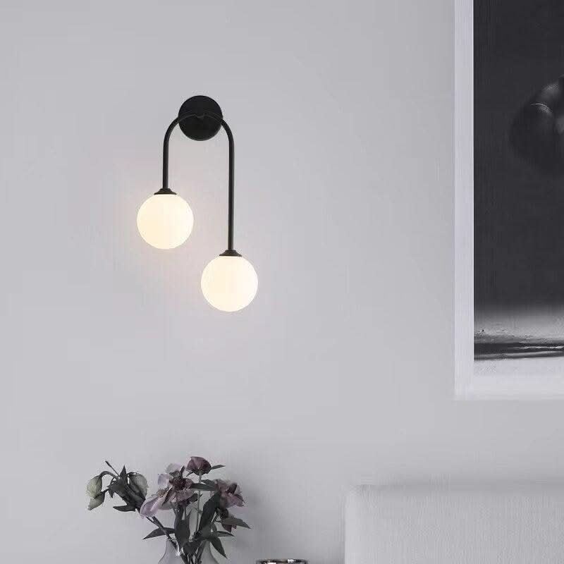 Version noire du luminaire double globe devant un mur clair, bouquet de fleurs séchées en bas