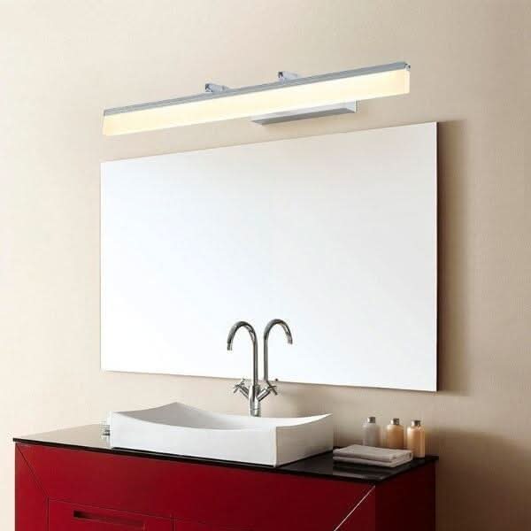 Applique chromée éclairant un miroir blanc au-dessus d'une vasque sur meuble rouge.