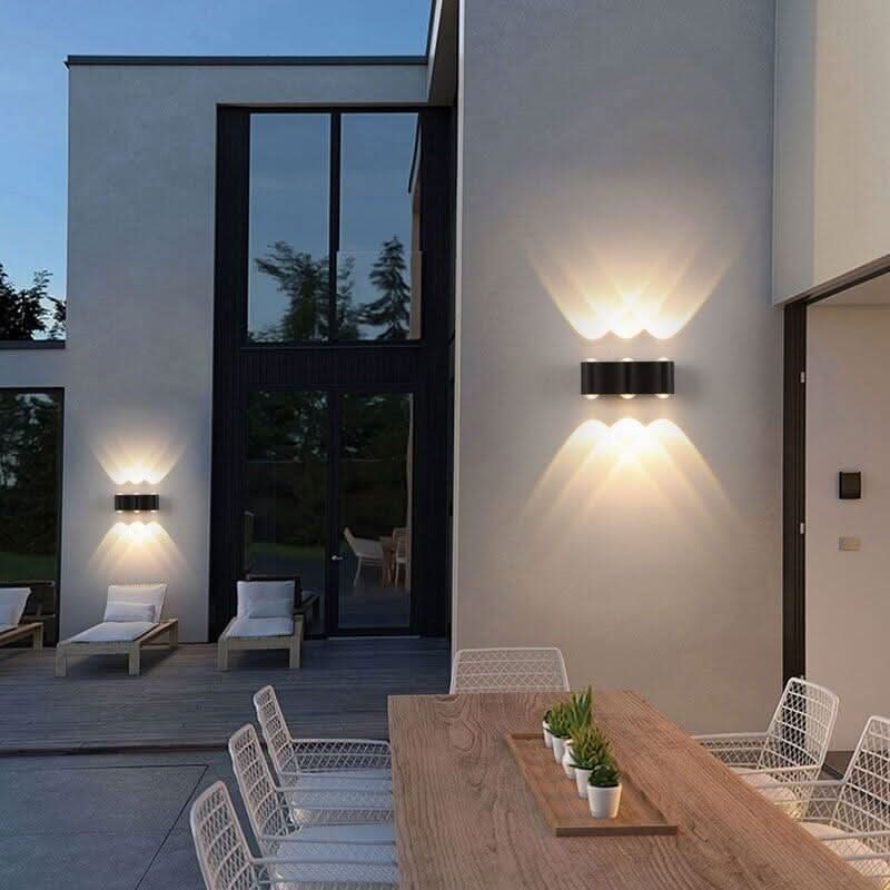 Deux appliques murales noires éclairant une terrasse extérieure au crépuscule, table et chaises.