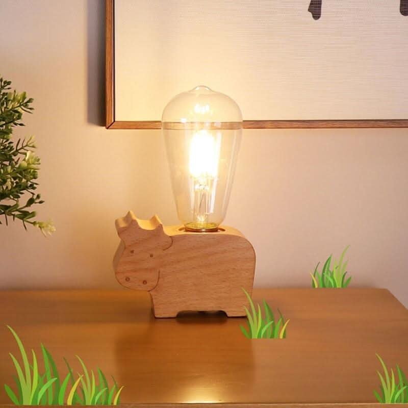 Lampe en bois en forme de vache allumée sur une table, cadre et herbe illustrée en arrière-plan.