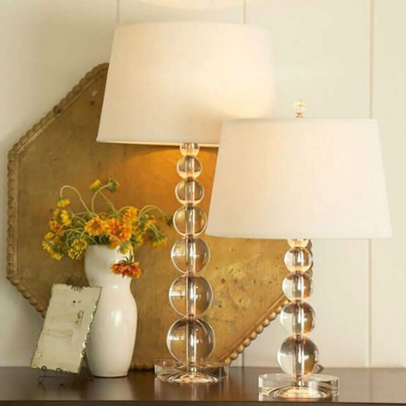 Deux lampes à poser en cristal devant un miroir doré, avec vase de fleurs jaunes.