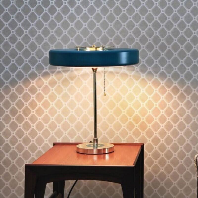 Lampe bleue allumée sur table en bois devant papier peint à motifs géométriques