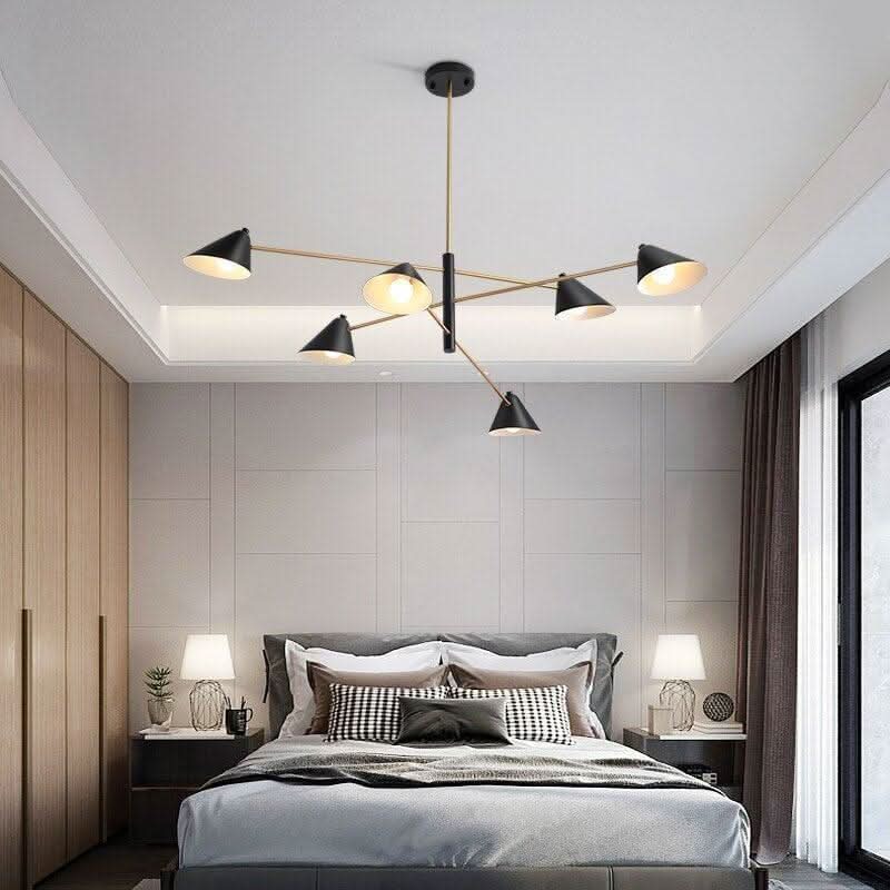 Chambre à coucher avec luminaire suspendu au-dessus du lit, abat-jours noirs et tiges dorées.