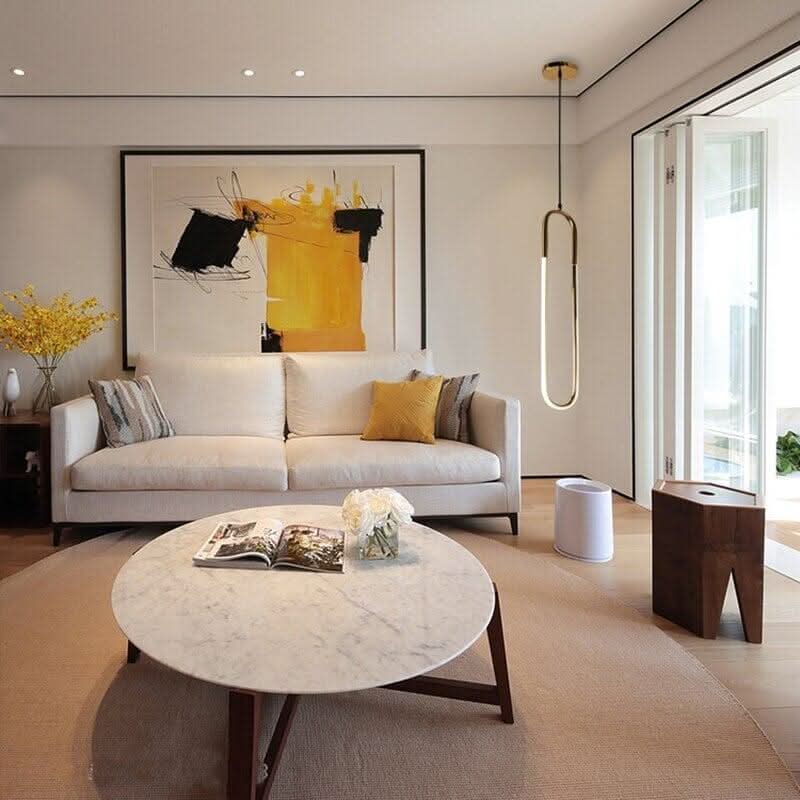 Mise en ambiance salon clair avec suspension verticale près de la baie vitrée.